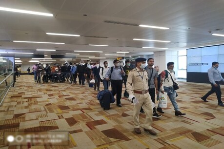 एयरोब्रिज पर प्रारंभिक स्वास्थ्य परीक्षण के बाद इमीग्रेशन जांच के लिए मुसाफिरों को ले जाते सीआईएसएफ के अधिकारी.