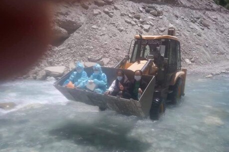 सांसद नामयाल की तरफ से जारी की गई तस्वीर में साफ नजर आ रहा है कि चार फ्रंटलाइन वर्कर एक अर्थ मूवर के आगे वाले हिस्से में बैठकर नदी पार कर रहे हैं. (फोटो: Twitter/@jtnladakh)