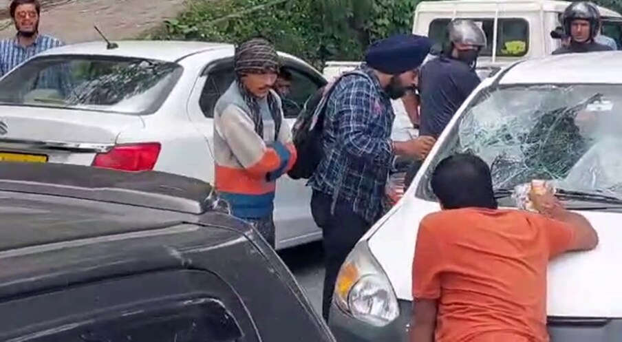  वीडियो में दिख रहा है कि एक शख्स ऑल्टो गाड़ी के आगे बोनट पर लेटा हुआ है और गाड़ी का फ्रंट शीशा टूटा हुआ है.