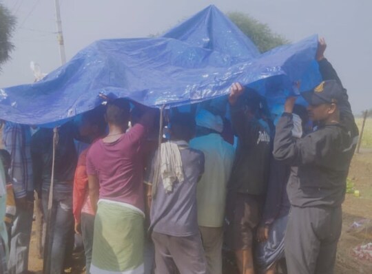 चिता के ऊपर तिरपाल लगाकर अंतिम संस्कार करते ग्रामीण