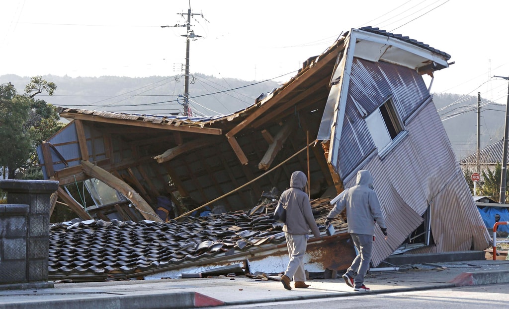People walk by a building collapsed following an earthquake in Shikamachi, Ishikawa prefecture, Japan Tuesday, Jan. 2, 2024. A series of powerful earthquakes in western Japan damaged homes, cars and boats, with officials warning people on Tuesday to stay away from their homes in some areas because of a continuing risk of major quakes and tsunamis. (Kyodo News via AP)