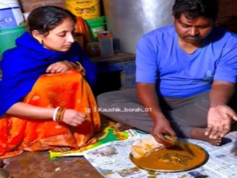 खाना खाते पति के पास बैठी हुई महिला (Image: Instagram/@kaushik_borah_01)