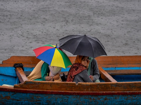 डल झील में बारिश के दौरान नाव से जाते स्‍थानीय लोग छाते की मदद से खुद को भीगने से बचाने की कोशिश कर रहे हैं. (फोटो: एपी)