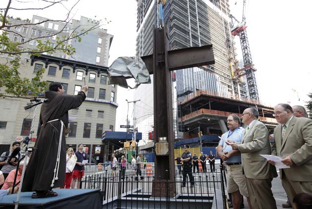 Father Brian Jordan (L), a Franciscan Priest, blesses The World Trade Center Cross, made of intersecting steel beams found in the rubble of buildings destroyed in the September 11 2001 attacks on the World Trade Center, before it is transported and lowered by a crane into an opening in the World Trade Center site below ground level where it will become part of the permanent installation exhibit in the 9/11 Memorial and Museum, in New York, July 23, 2011. Frank Silecchia (3rd R), a construction worker who found the cross, former New York Mayor Rudy Giuliani (2nd R) and Richard Sheirer (R), director of the Office of Emergency Management listen to the prayer. The 9/11 Memorial and Museum at the World Trade Center site will open on the 10 year anniversary of the attacks on September 11, 2011.