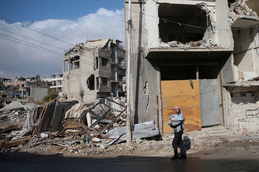 A man carries a baby near damaged buildings in the rebel held besieged city of Douma, in the eastern Damascus suburb of Ghouta, Syria (REUTERS)