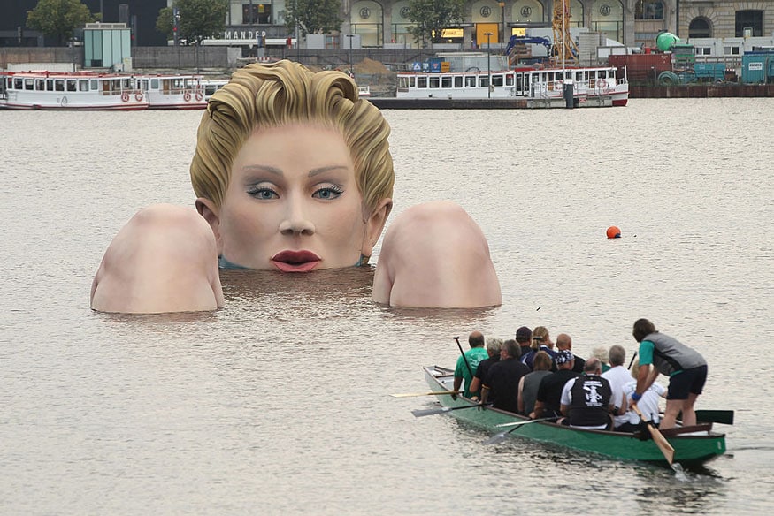 Men in a boat approach 'Die Badende' ('The Bather'), a giant sculpture showing a woman's head and knees as if she were resting in the Binnenalster lake on August 3, 2011 in Hamburg, Germany. The sculpture, which is made of styrofoam and steel and measures 4 meters high and 30 meters long, is a project by artist Oliver Voss and will be on display for the next ten days. (Image: Getty Images)