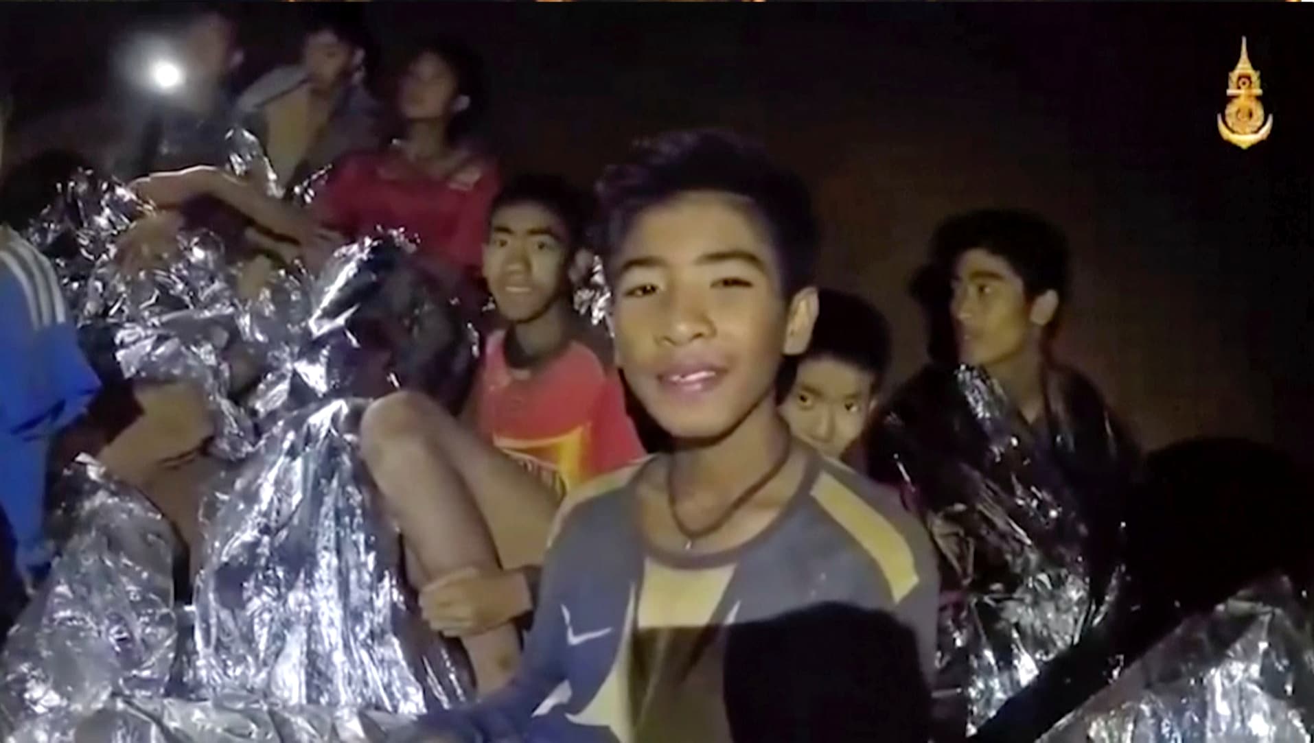 In this July 3, 2018, image taken from video provided by the Royal Thai Navy Facebook Page, Thai boys smile as Thai Navy SEAL medic help injured children inside a cave in Mae Sai, northern Thailand.  The Thai soccer teammates stranded more than a week in the partly flooded cave said they were healthy on a video released Wednesday, as heavy rains forecast for later this week could complicate plans to safely extract them. (Royal Thai Navy Facebook Page via AP)