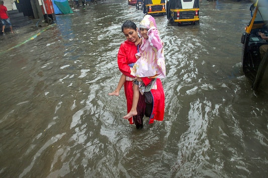 A woman, carrying a girl, wades through a waterlogged road during heavy rains, in Thane. (Image: PTI) A woman, carrying a girl, wades through a waterlogged road during heavy rains, in Thane. (Image: PTI)