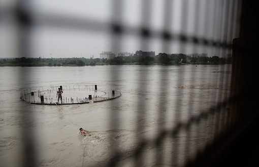 An Indian man swims to reach an under-construction pillar submerged in the river Yamuna in New Delhi. (Image: AP)