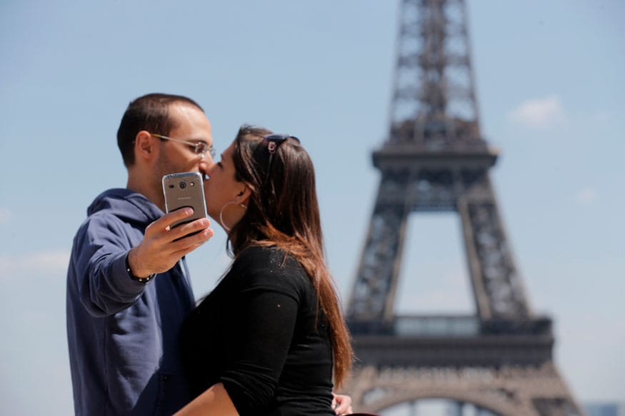 A couple of tourists use a mobile phone to take a selfie picture as they kiss at the Trocadero Square near the Eiffel Tower in Paris. (Image: Reuters)