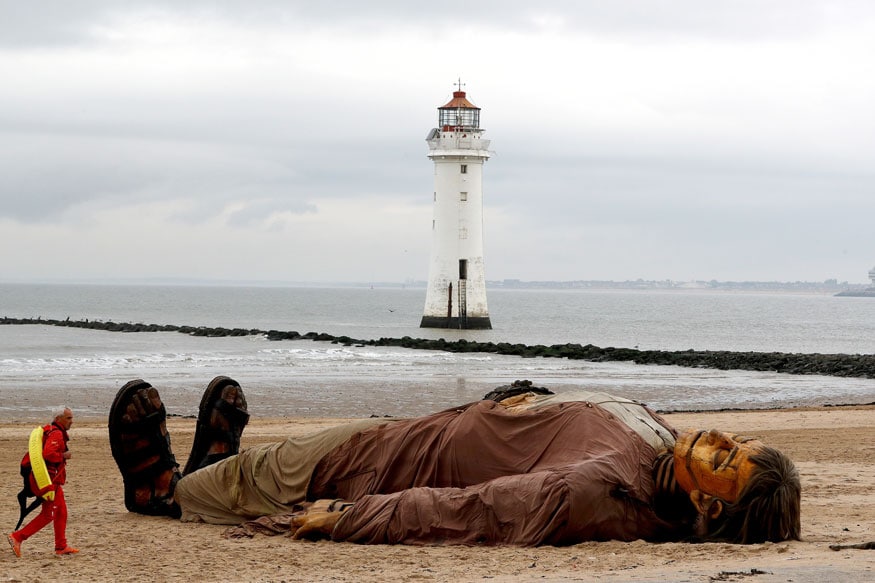 A lifeguard passes one of Royal Deluxe's giant marionette puppets as it lies on the beach at New Brighton, Britain. (Image: Reuters)