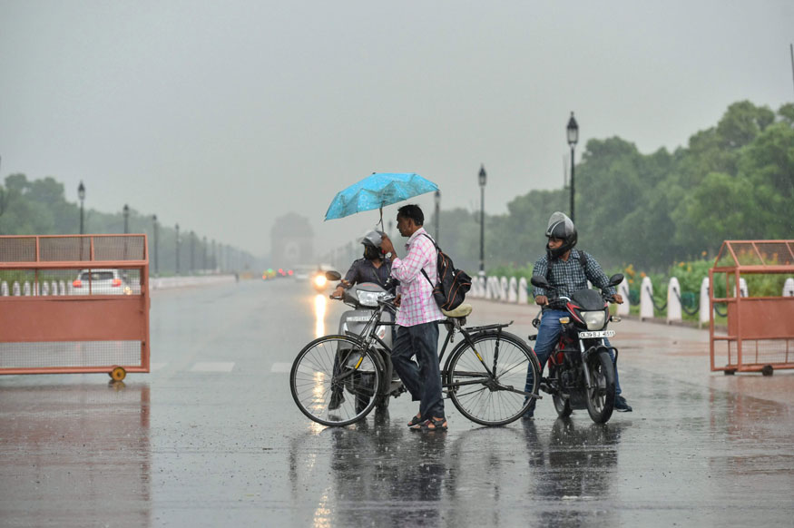 A cyclist holding an umbrella crosses a road during rainfall, in New Delhi. (Image: PTI)
