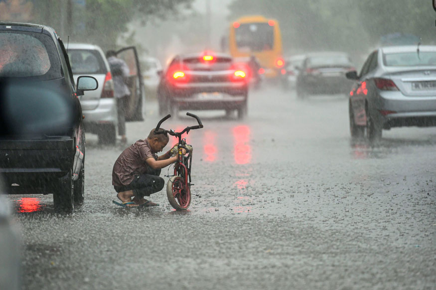 A boy repairs his cycle as vehicles ply at a road during rains in New Delhi. (Image: PTI)