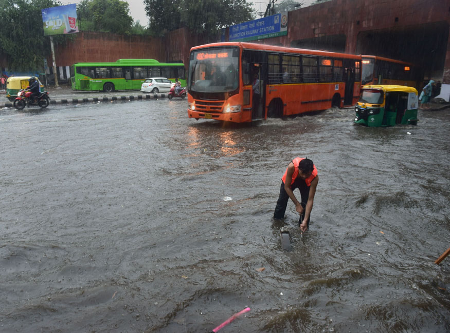 A civic worker opens a pothole to clear the rain water accumulated on a road during a downpour in New Delhi. (Image: PTI)