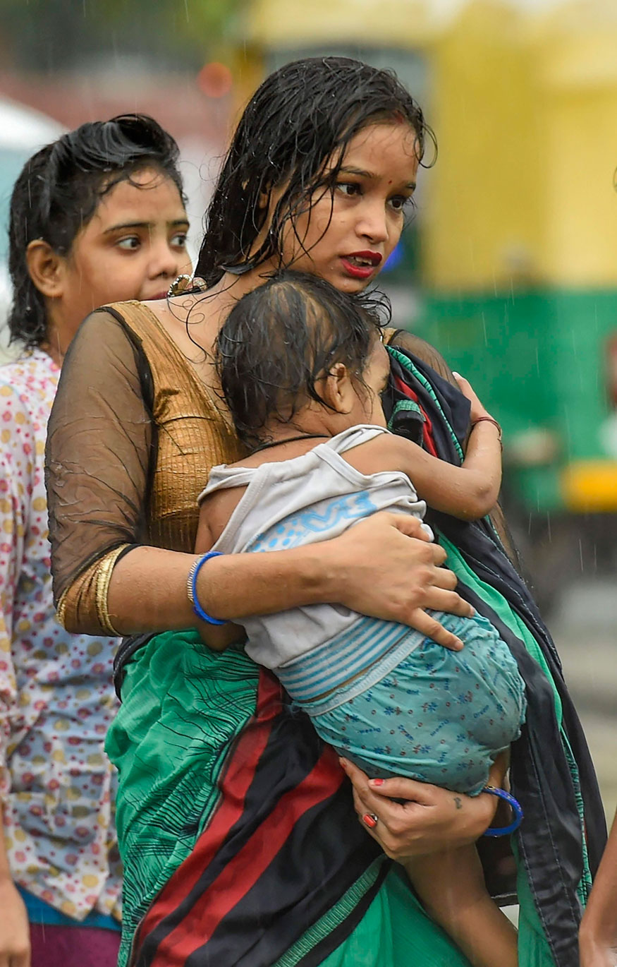A woman carries a child during rains in New Delhi. (Image: PTI)