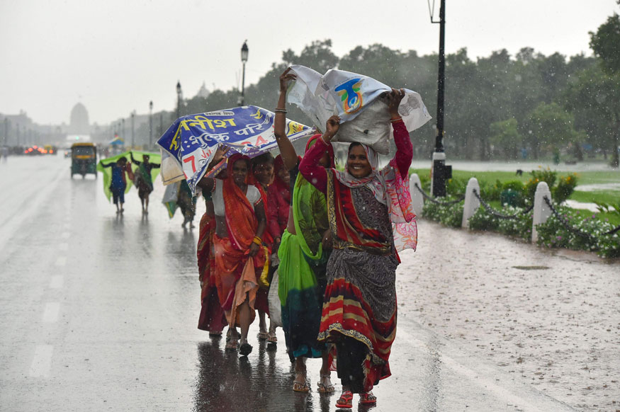Women try to cover themselves with plastic banners as they walk along the Rajpath during rains, in New Delhi. (Image: PTI)