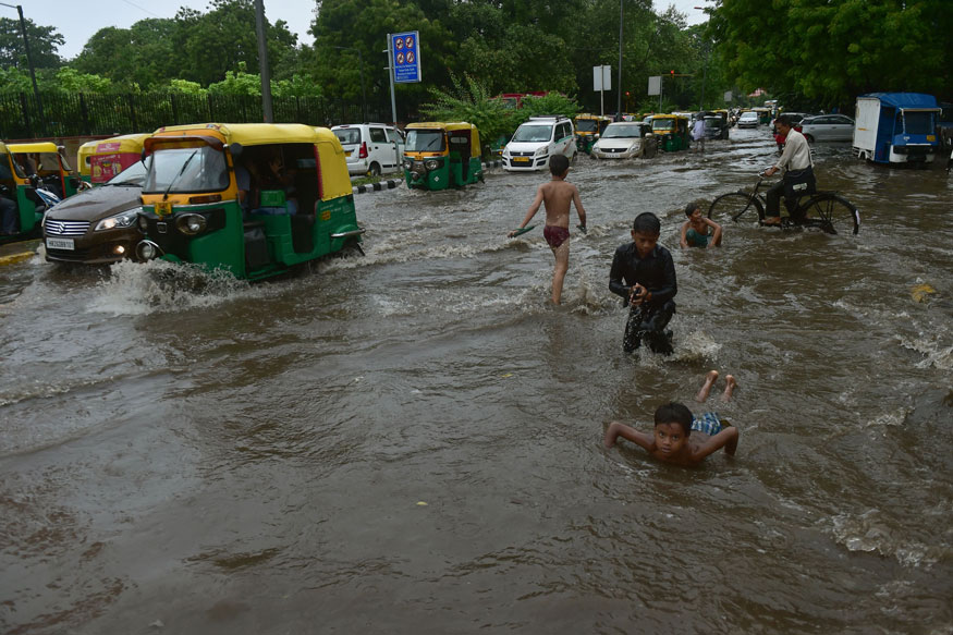 Children play while vehile ply at a waterlogged road after rains, in New Delhi. (Image: PTI)
