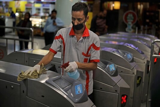 A worker disinfects the gates as a precaution against COVID-19 at a metro station in New Delhi. (Image: AP)