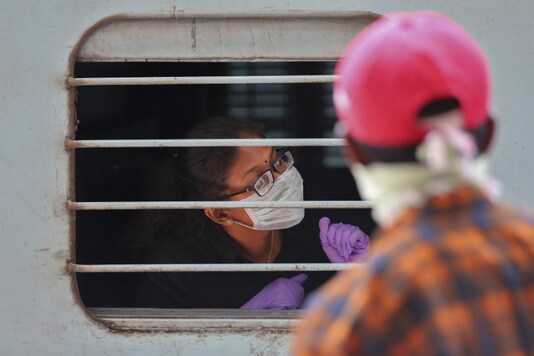 A passenger wearing face mask and gloves as a precaution against COVID-19 peeps out of a train window at Secunderabad Railway Station. (AP Photo/Mahesh Kumar A.)