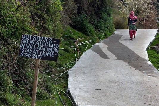 A sign at the entrance of a village reads 'Outsiders aren't allowed in Village Naddi - stay home-stay safe' as a woman walks out of Naddi village in Dharmsala, Himachal Pradesh. (PTI)