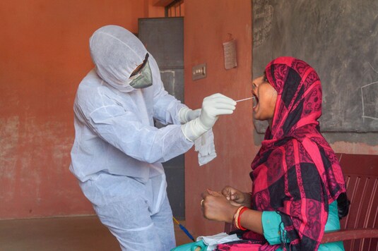 A medic collects swab from the mouth of a woman for COVID-19 test at a camp organised at a government school, during the nationwide lockdown. (Image: PTI)