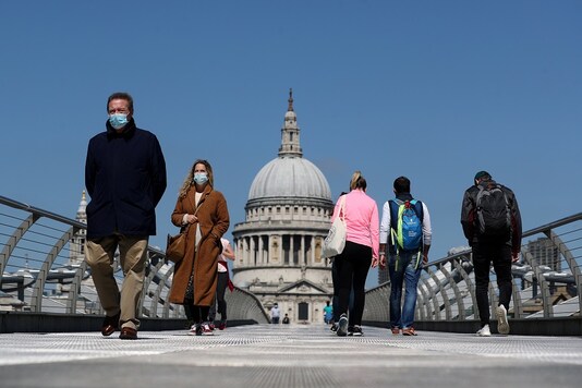 People wearing face masks cross Millennium Bridge, as the spread of the coronavirus disease (COVID-19) continues, in London. (Reuters)