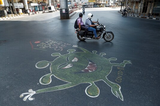 People ride past a graffiti on a road depicting the coronavirus in Mumbai. (Reuters)