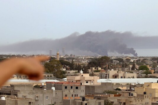 A finger points at smoke rising above buildings in the Libyan capital Tripoli, during reported shelling by strongman Khalifa Haftar's forces, on May 9, 2020. Mahmud TURKIA / AFP