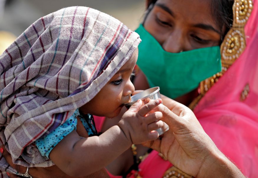  A child of a migrant worker drinks water as his mother holds him while waiting in a queue for transport to reach to a railway station to board a train to their home state of northern Uttar Pradesh, after a limited reopening of India's giant rail network following a nearly seven-week lockdown to slow the spreading of the coronavirus disease (COVID-19), in Ahmedabad. (Image: Reuters)