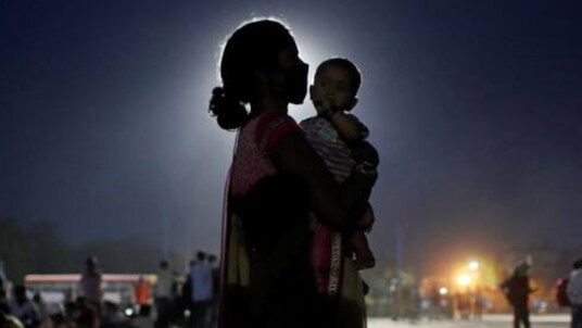A woman and her baby wait for a bus to take them to a railway station to board a train to their home state of Uttar Prades,in the outskirts of New Delhi. (Image: Reuters)