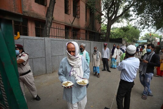 An impoverished man walks after receiving food prepared by the Bangla Sahib Gurdwara kitchen as others wait in a queue in New Delhi. (AP Photo)