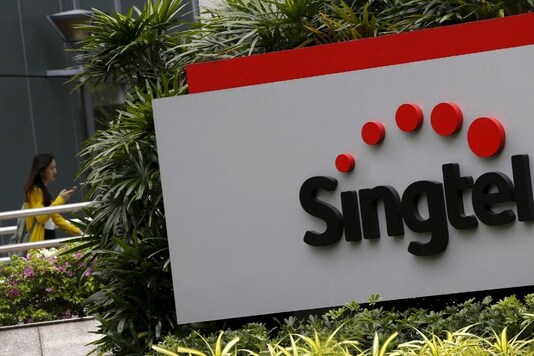 FILE PHOTO: A woman using a mobile phone walks behind a Singtel signage at their head office in Singapore February 11, 2016. REUTERS/Edgar Su
