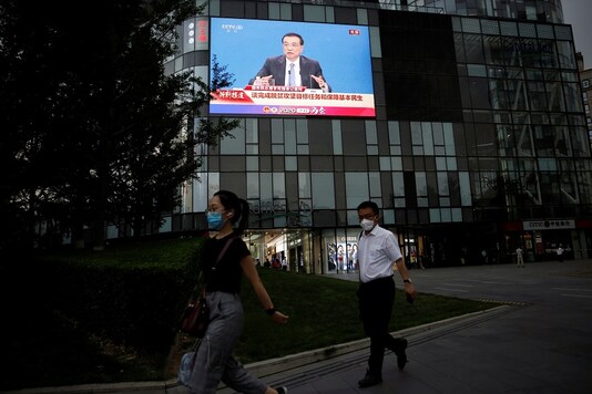 People wearing face masks following the coronavirus disease (COVID-19) outbreak walks past a giant screen showing a news conference by Chinese Premier Li Keqiang after the closing session of the National People's Congress, outside a shopping mall in Beijing on Thursday. (Reuters)