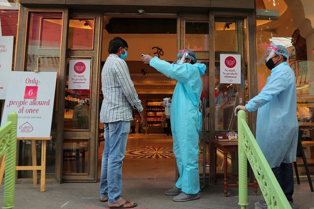An Indian security personnel wearing protective gear checks the temperature of a customer before allowing him to enter a sweet shop in Hyderabad, India, Friday, June 5, 2020. (AP Photo/Mahesh Kumar A.)