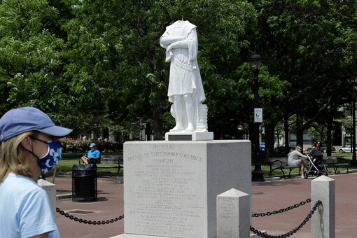 A passer-by walks near a damaged Christopher Columbus statue, Wednesday, June 10, 2020, in a waterfront park near the city's traditionally Italian North End neighborhood, in Boston. The statue was found beheaded Wednesday morning, Boston Mayor Marty Walsh said.  (AP Photo/Steven Senne)