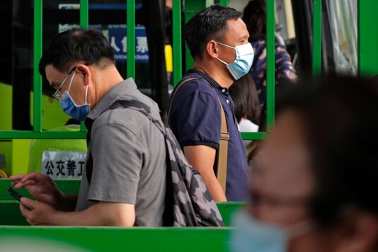 Commuters wearing protective face masks to help curb the spread of the new coronavirus line up to board a bus at a bus terminal in Beijing,  2020. (AP Photo/Andy Wong)