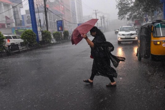 A woman in Kerala crosses a road holding an umbrella against a heavy downpour and wind. (Photo: PTI)