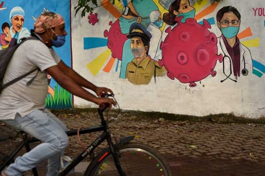A man wearing a mask pedals his bicycle past a graffiti on a wall made to create awareness about the coronavirus. (AP)