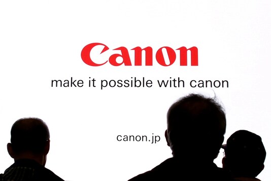 People are silhouetted against a display of the Canon brand logo at the CP+ camera and photo trade fair in Yokohama, Japan, REUTERS/Thomas Peter/File Photo