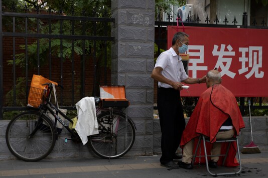 A street barber wearing a face mask to protect against the coronavirus attends to his customer near a banner on the pandemic which reads 