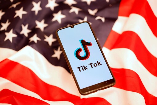 The logo of the much-controversial TikTok app is seen on a smartphone, against the backdrop of the national flag of the United States of America. (Image: Reuters)