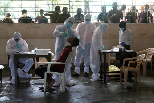 A health worker in personal protective equipment (PPE) collects a swab sample from a man as people outside wait for their test results during a rapid antigen testing check up campaign for the coronavirus disease (COVID-19), at a school in Mumbai, India, August 8, 2020. REUTERS/Francis Mascarenhas