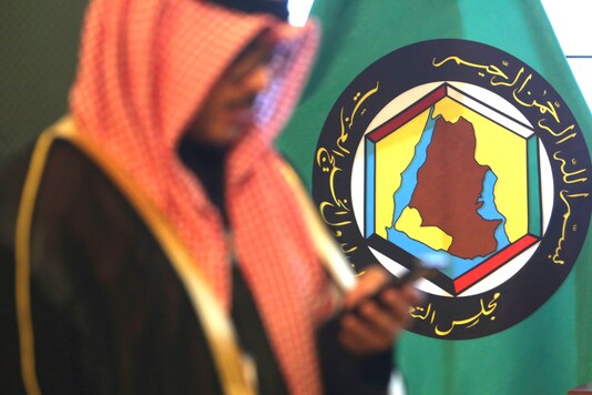 FILE - In this Dec. 5, 2017 file photo, a man looks at his mobile phone in front of the flag of the Gulf Cooperation Council, GCC, in Kuwait City. The GCC, a six-nation bloc of Gulf Arab nations torn apart by internal strife, unanimously endorsed on Sunday, Aug. 9, 2020, an extension of a United Nations arms embargo on Iran, just two months before it is set to expire. (AP Photo/Jon Gambrell, File)
