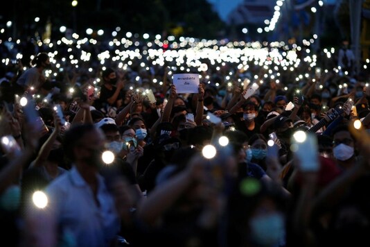 Pro-democracy protesters use mobile phones as flashlights at a rally as one of them is holding a placard at a rally to demand the government to resign, to dissolve the parliament and to hold new elections under a revised constitution, near the Democracy Monument in Bangkok, Thailand, August 16, 2020. REUTERS/Soe Zeya Tun
