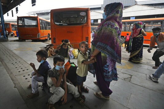 एक प्रवासी मजदूर परिवार अपने बच्चों के साथ परिवहन की प्रतीक्षा करता है क्योंकि वे नई दिल्ली में काम के लिए शहर लौटते हैं।  (एपी)