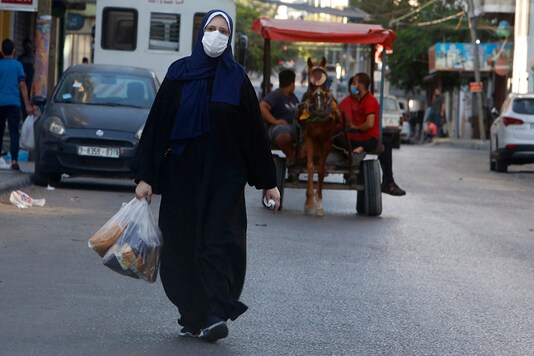 A Palestinian women wears a face mask carries her shopping during a lockdown imposed following the discovery of coronavirus cases in the Gaza Strip, Thursday, Aug. 27, 2020. (AP Photo/Hatem Moussa)