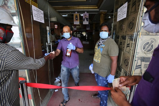 Salespersons handover liquor bottles to customers at the entrance of their outlet during a lockdown to curb the spread of new coronavirus, in Bangalore, on May 6, 2020. (AP Photo/Aijaz Rahi) 