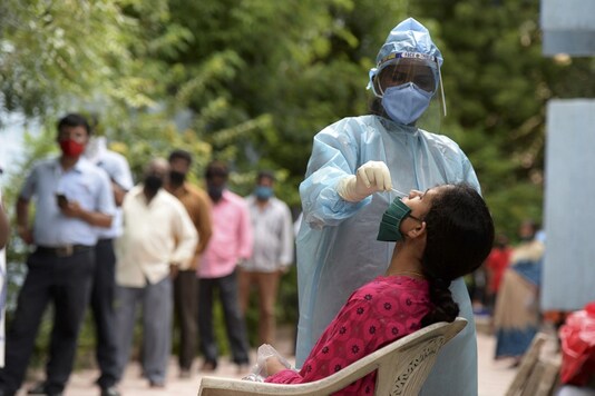 Residents stand in a queue to register their names as a health worker wearing PPE suit collects a swab sample from a woman to test for Covid-19. (Photo by NOAH SEELAM / AFP)