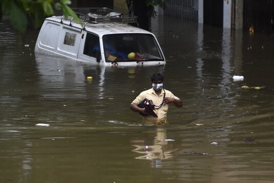 A man wades through a flooded street next to a partially submerged van following heavy monsoon rains in Mumbai on September 23, 2020. (Punit PARANJPE / AFP)