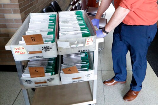 FILE - In this May 5, 2020, file photo, absentee ballots to be counted are moved at City Hall in Garden City, Mich. Data obtained by The Associated Press shows Postal Service districts across the nation are missing the agencys own standards for on-time delivery as millions of Americans prepare to vote by mail. (AP Photo/Paul Sancya, File)